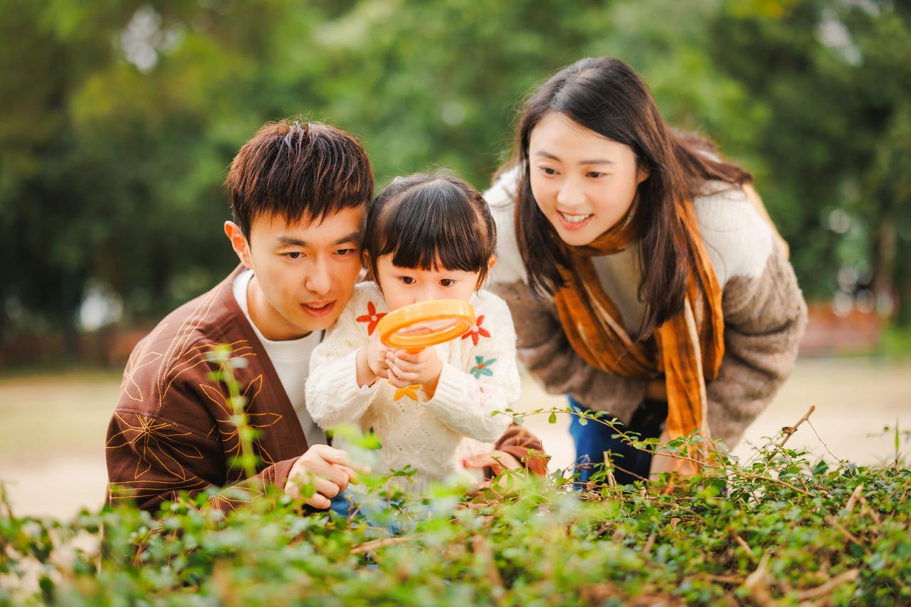 A couple doing an exploration with their young child with a magnifying glass in the park
