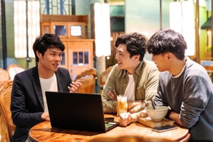 Man showing his laptop to a group of friends in a café