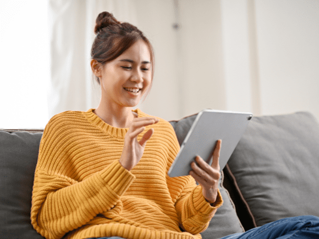 Woman in an orange sweater is happily browsing on her tablet