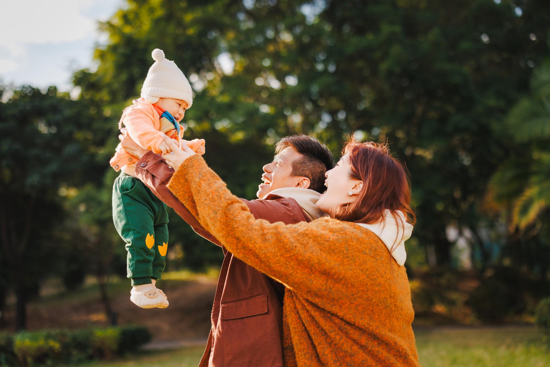 A_couple_holding_up_their_baby_happily_in_the_air_in_the_park_(1).jpg