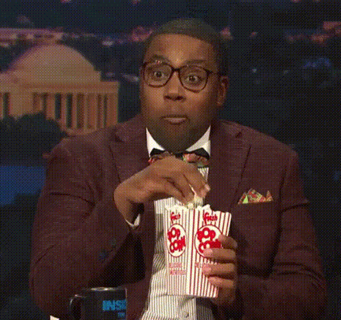 Man in glasses eating popcorn and nodding
