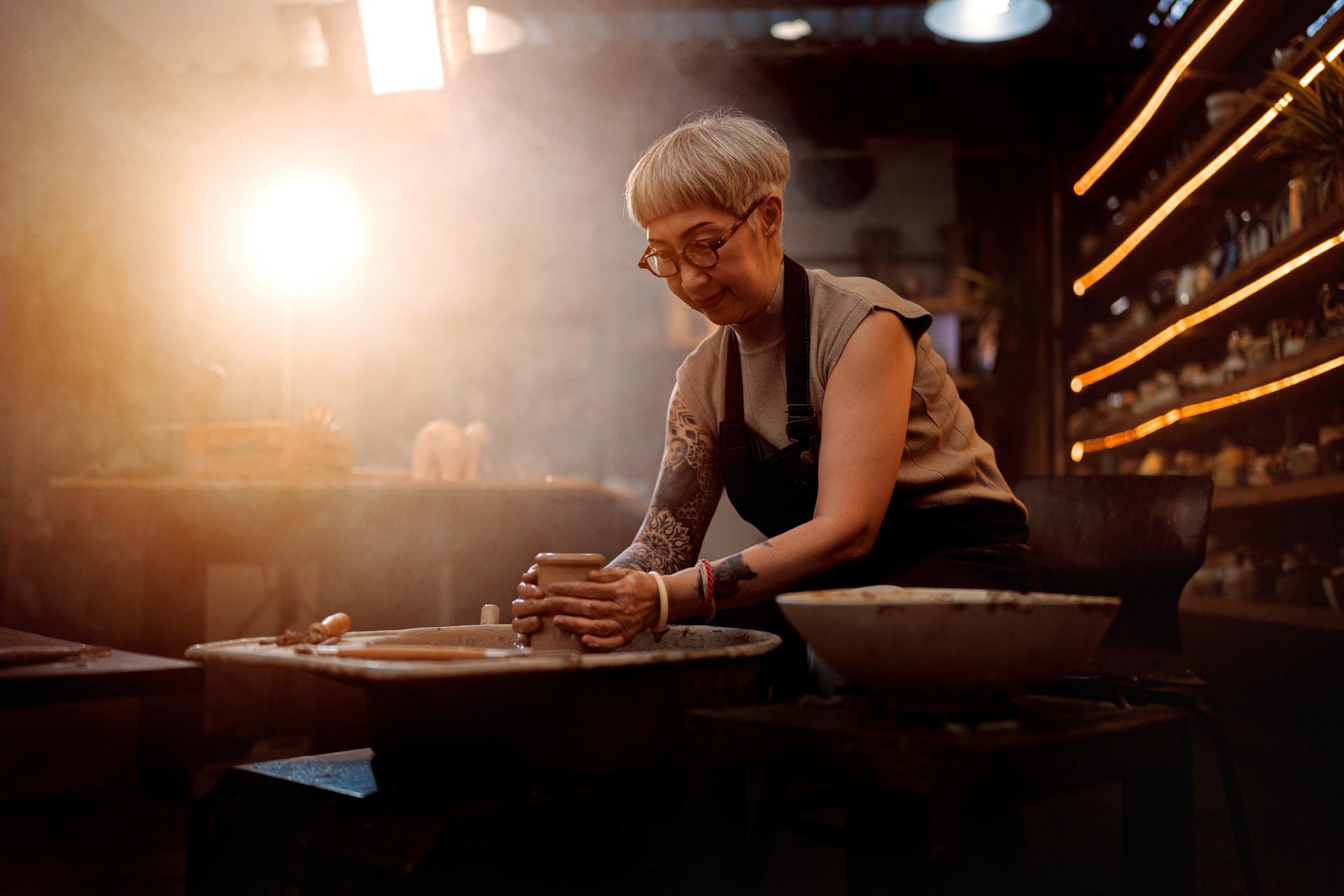 Senior artist woman making clay bowl on pottery wheel in studio