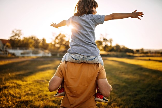Father carrying his child on his shoulders as they face the Sun