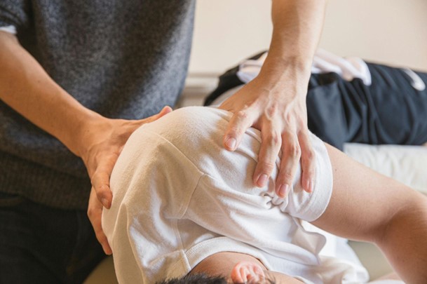 A patient receiving a shoulder massage from a physical therapist who is gently touching the man's shoulder during a physiotherapy session.