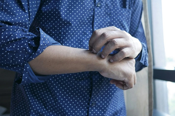 A man in a blue shirt with white polka dots is adjusting his wrist, possibly due to an itch.
